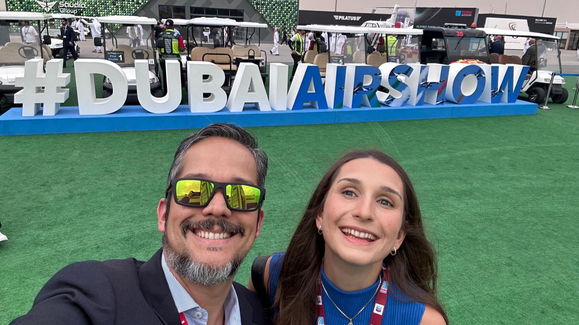 Man and woman taking a selfie in front of a sign that reads #DubaiAirshow