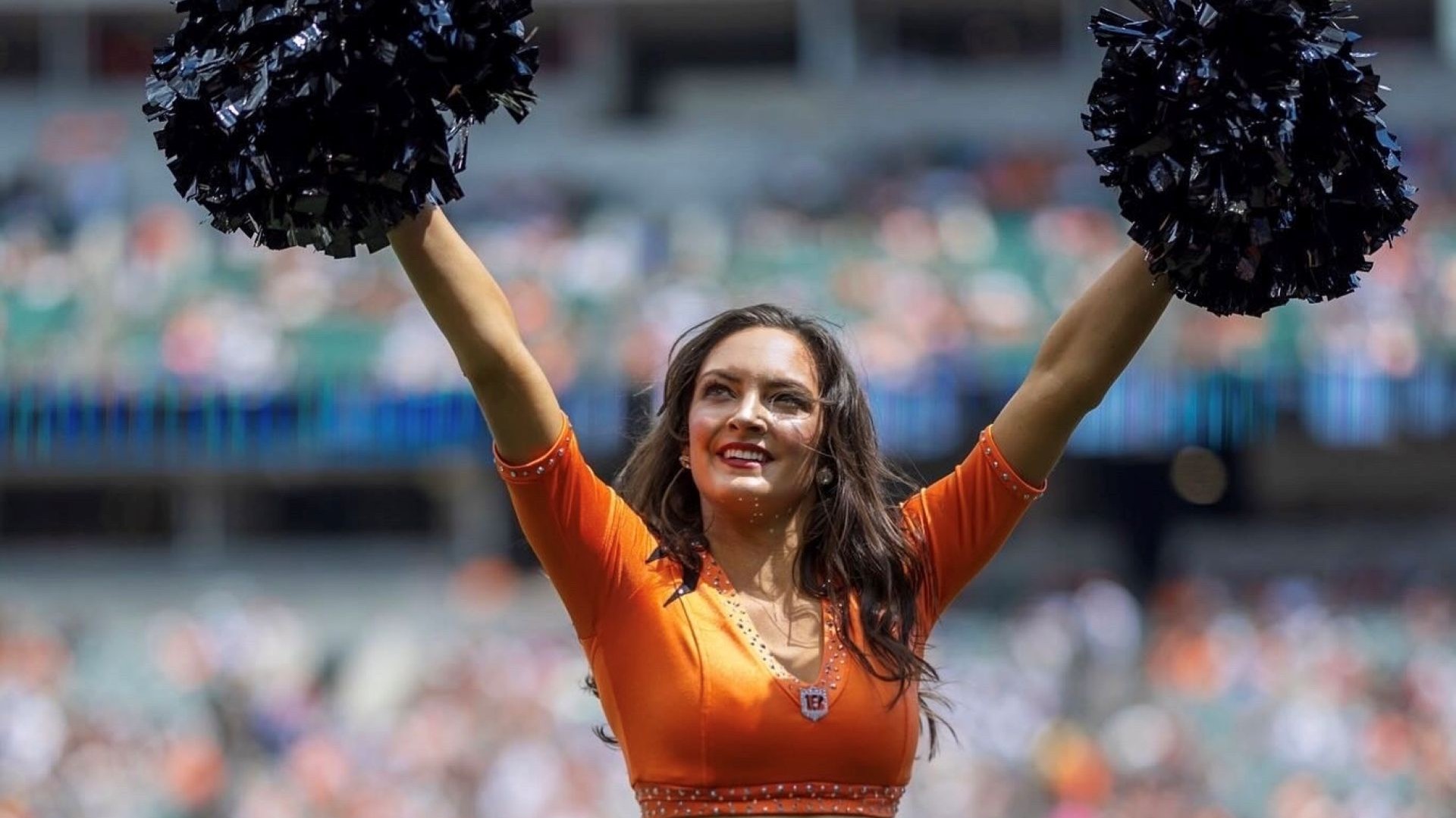 Woman standing in an orange uniform on a football field holding pom-poms