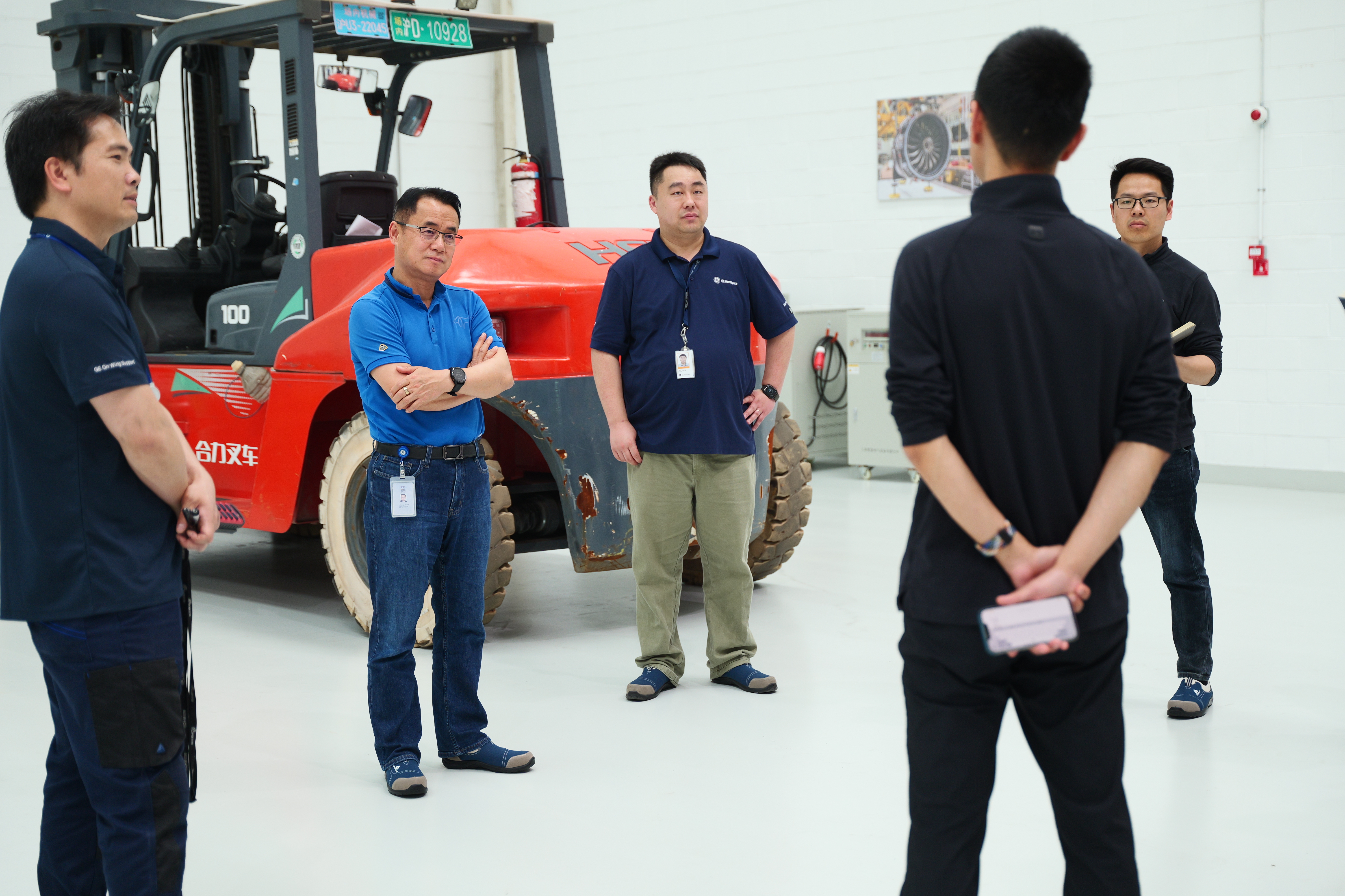 5 men in a workshop with a large red forklift behind them