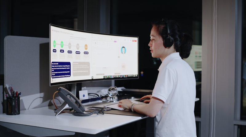 A woman standing before a large monitor and typing