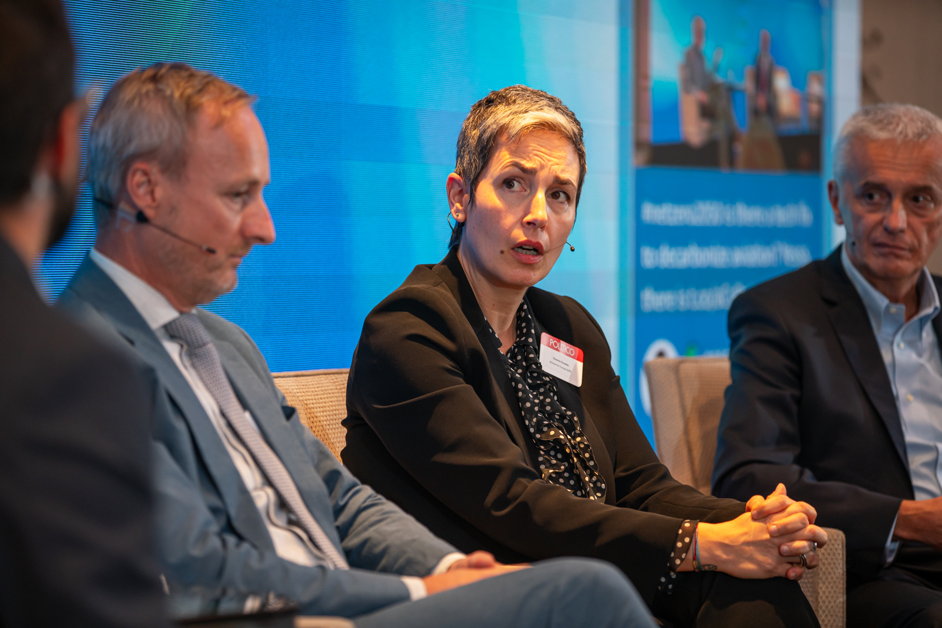 Two men and one woman in suits on a panel