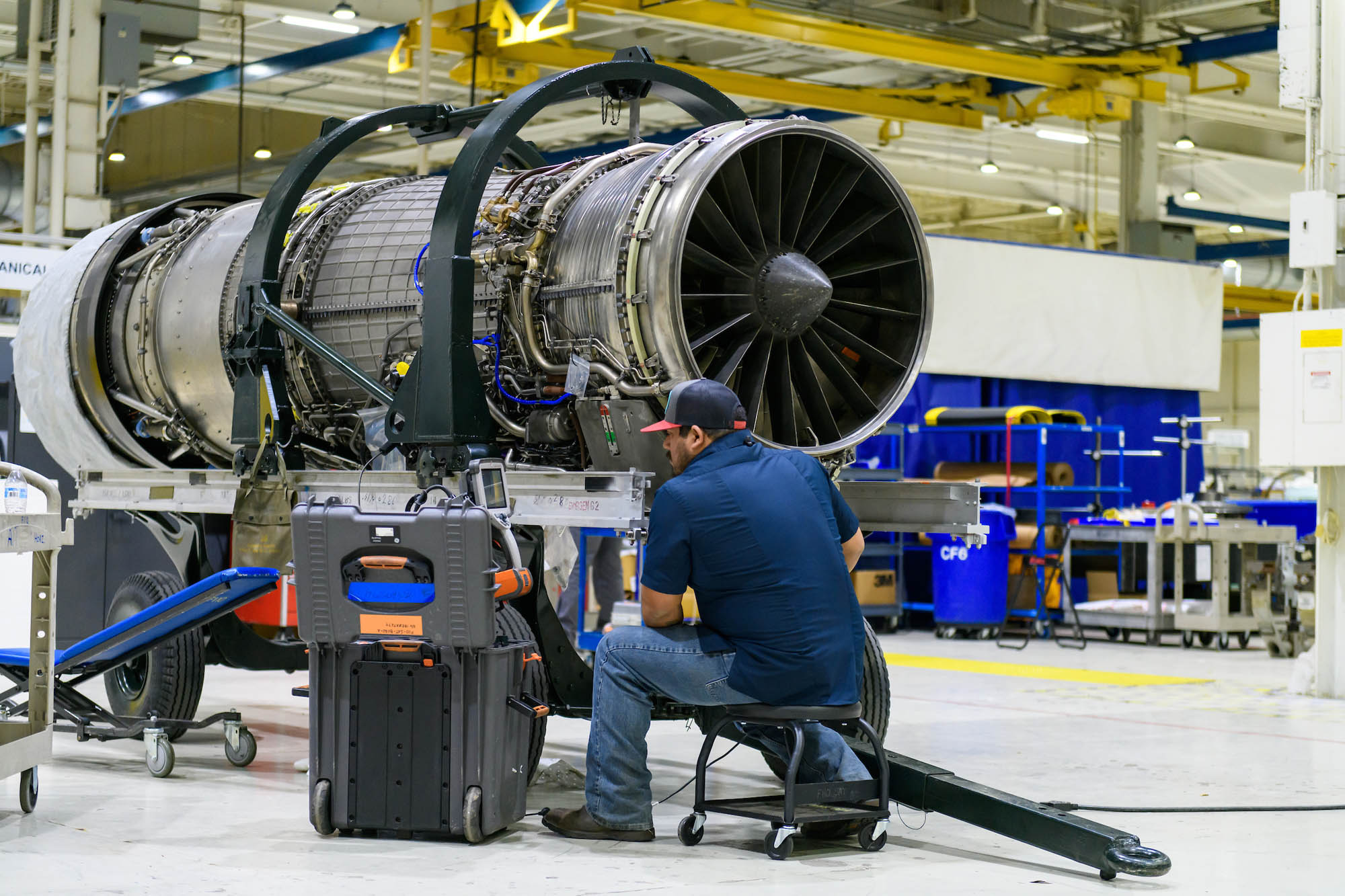 An F-110 engine being worked on by a man on a stool