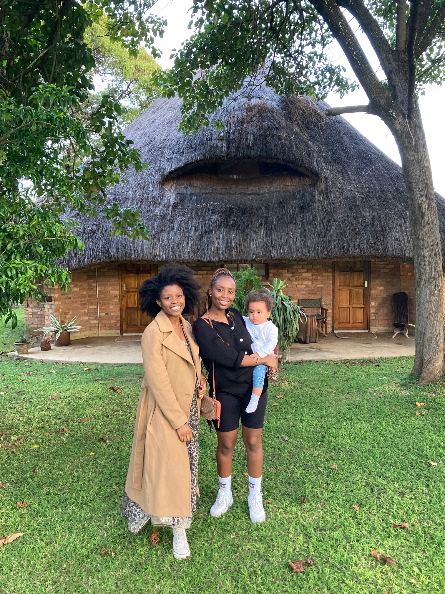 two women and a baby in front of a thatched house