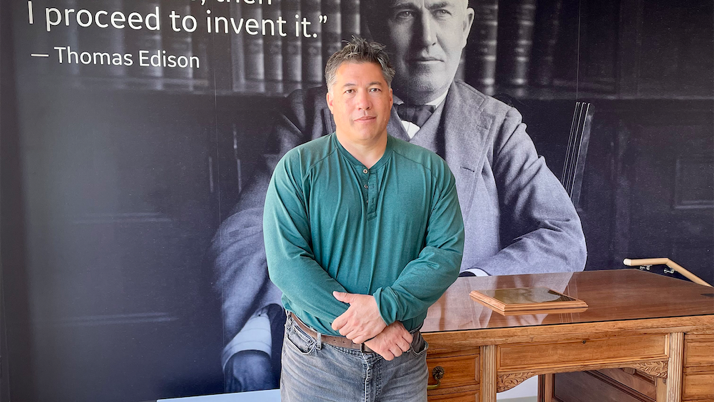 Peter Tu standing in front of an image of Thomas Edison