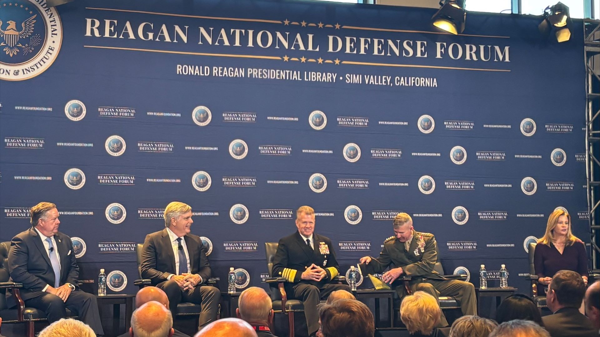 Panel of 4 men and one woman in front of blue backdrop